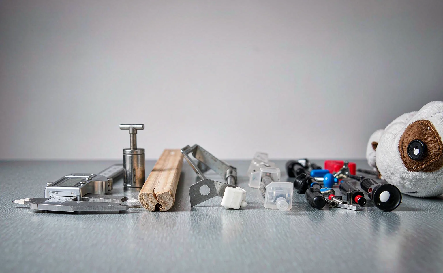 Rejected baby crib components on the inspection bench — cracked wooden slat, loose plastic parts, a detached plush eye, a digital caliper and a small-parts gauge