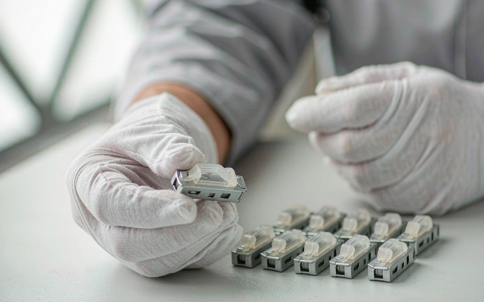 Hands in white gloves sorting small metal parts on an inspection bench