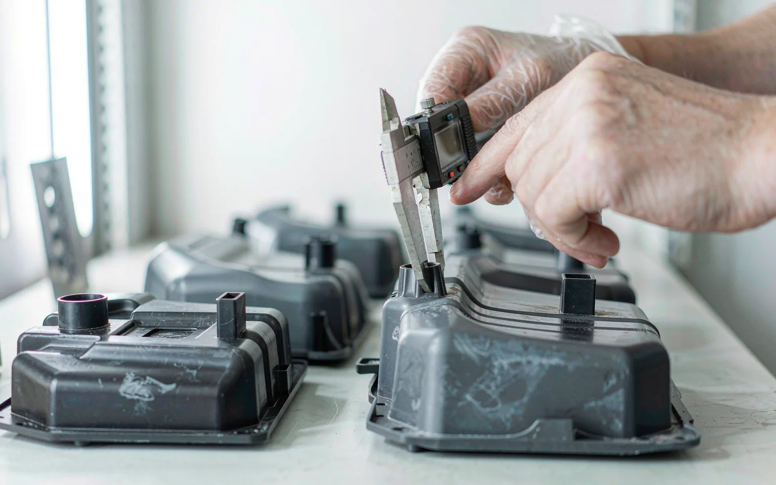 Molded plastic electronic housings and enclosures laid out on a bench while an inspector measures a moulded rib with a digital caliper