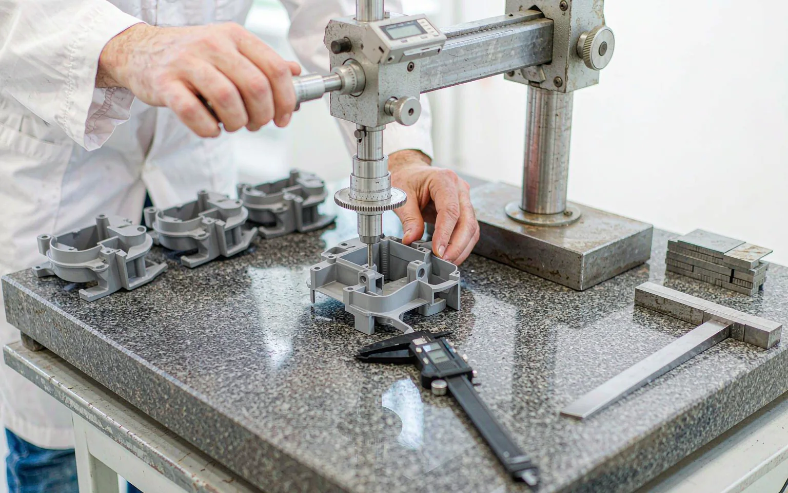 Engineer measuring a first-article molded part on a granite surface plate with a height gauge and caliper