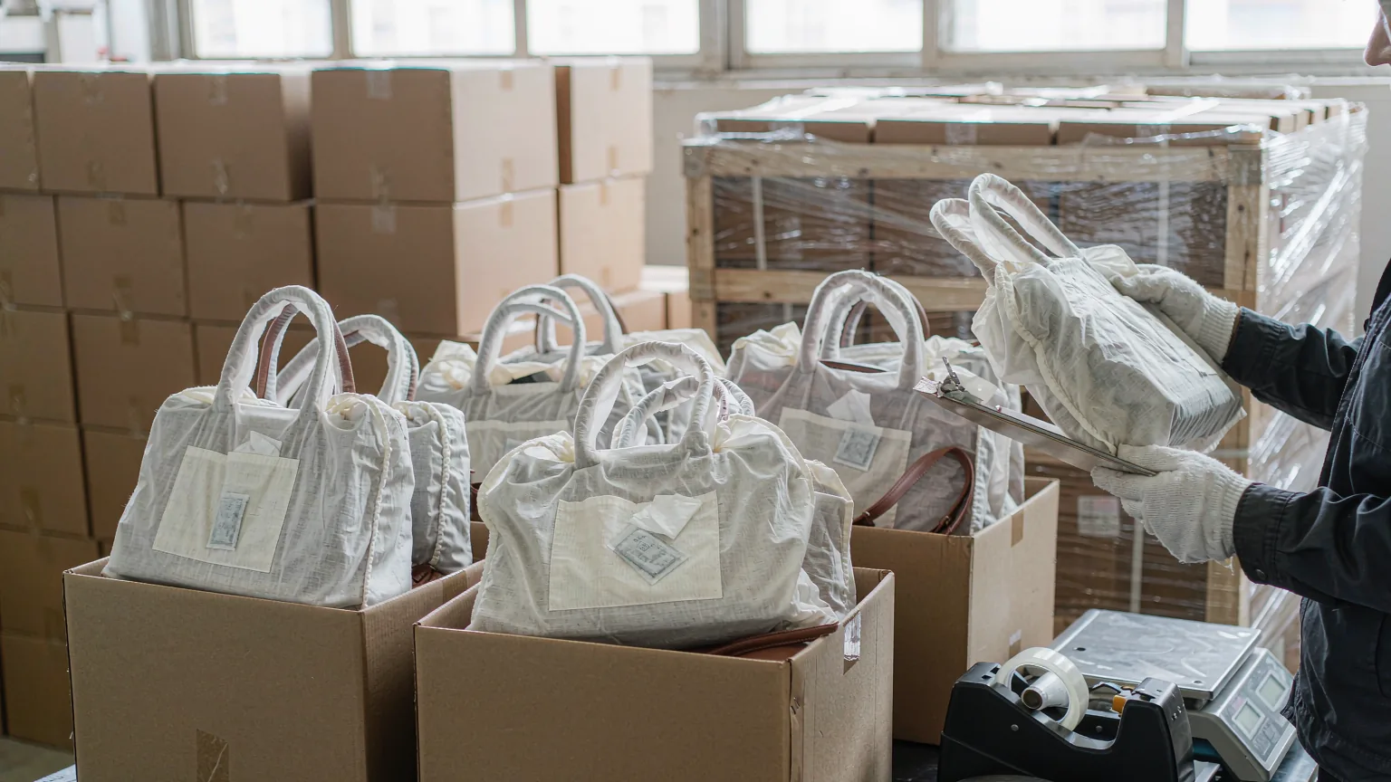 UTS inspector checking leather handbags packed in dust bags inside open export cartons before a final random inspection