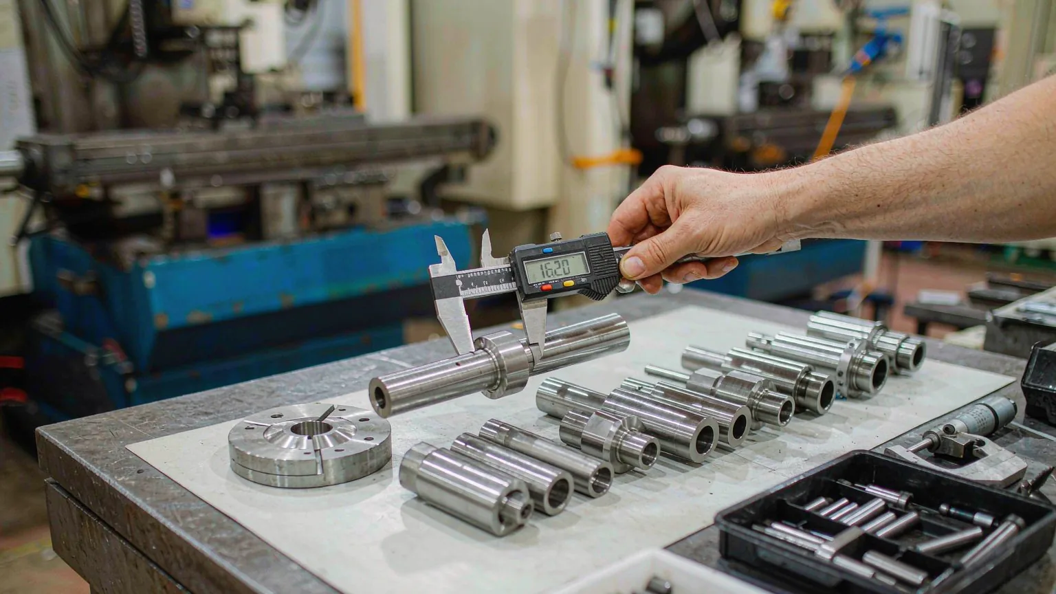 UTS inspector measuring CNC-machined steel shafts and flanges with a digital caliper at the workbench
