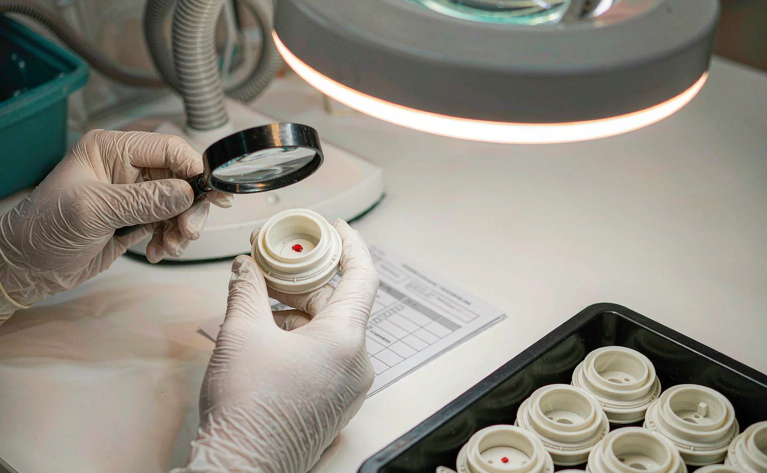 Inspector examining a molded plastic sample with a magnifier against the specification