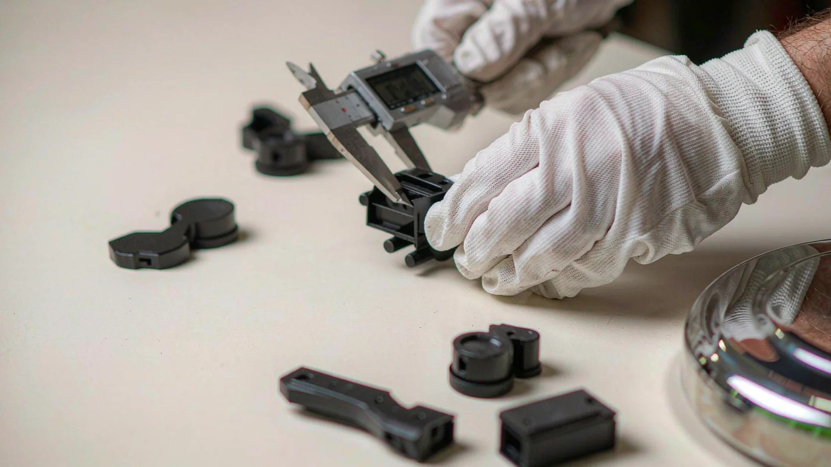 Hands in white gloves measuring first-article moulded parts with a caliper