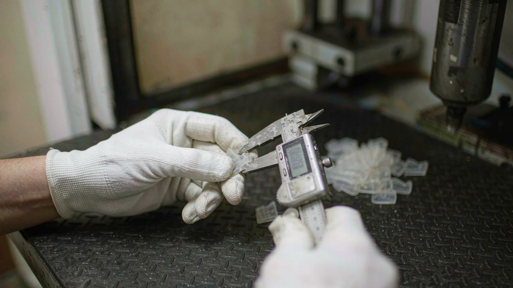 Hands in white gloves measuring small moulded components with a caliper